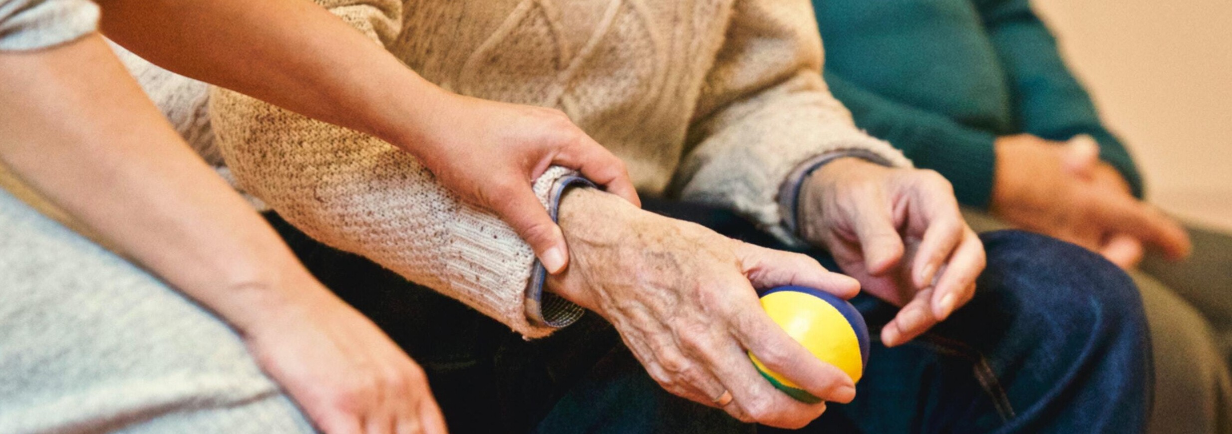 Close up of woman's hand resting on forearm of elderly man holding a strength ball