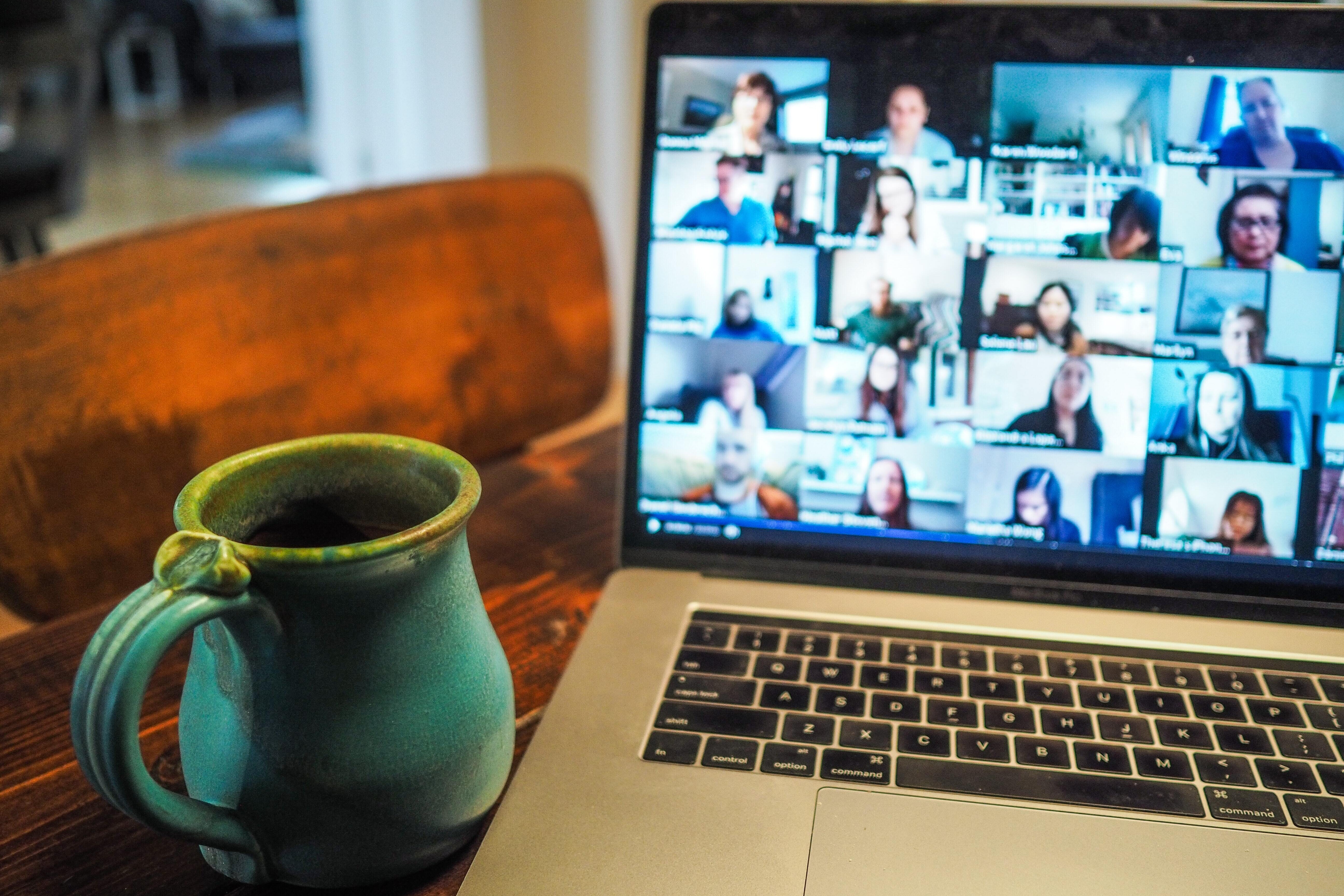 Closeup open laptop showing multiple person video conference and green ceramic coffee mug on wooden table
